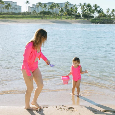 Woman in a SwimZip neon pink high waist swim bottom plays with her daughter at the beach—What is high-visibility swimwear?
