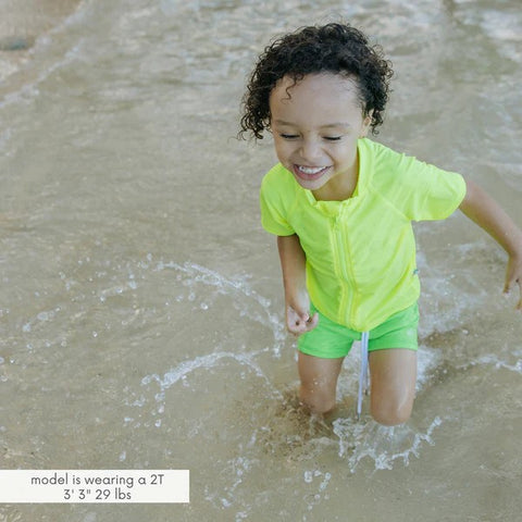 Boy in a SwimZip short-sleeved rash guard plays at the beach—What is high-visibility swimwear?