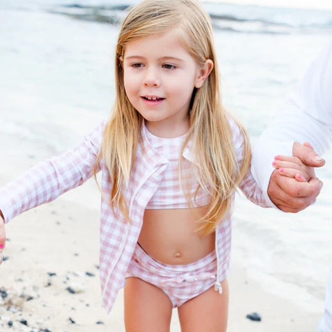 Girl in a SwimZip pink gingham rash guard plays at the beach—Best swimsuits.