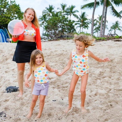 Girl in a SwimZip ruffle one-piece swimsuit playing at the beach with her mom and little sis—Best swimsuits.