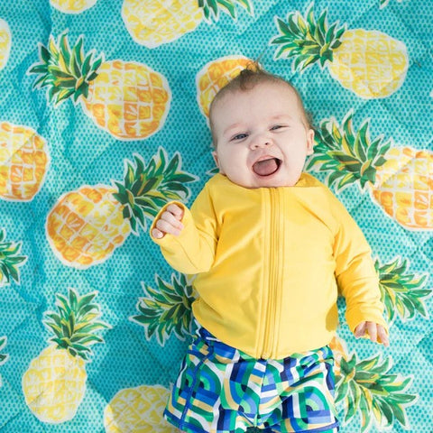 Baby boys in a SwimZip yellow rash guard lies on the beach—Best swimsuits.