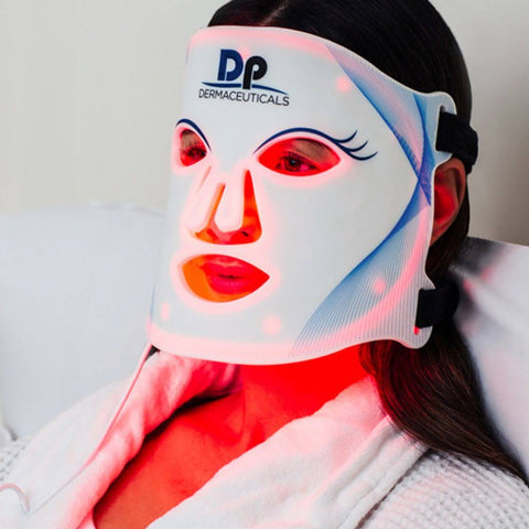 A person relaxing with a DP DermaCeuticals LED facial mask emitting red light, targeting anti-aging skin care therapy for face rejuvenation.