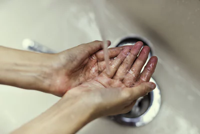 washing both hands under running water from a faucet