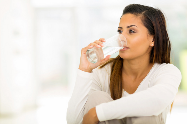 woman wearing white long sleeves drinking a glass of water