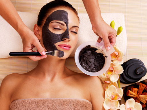 girl lying down with someone applying black mask on her face