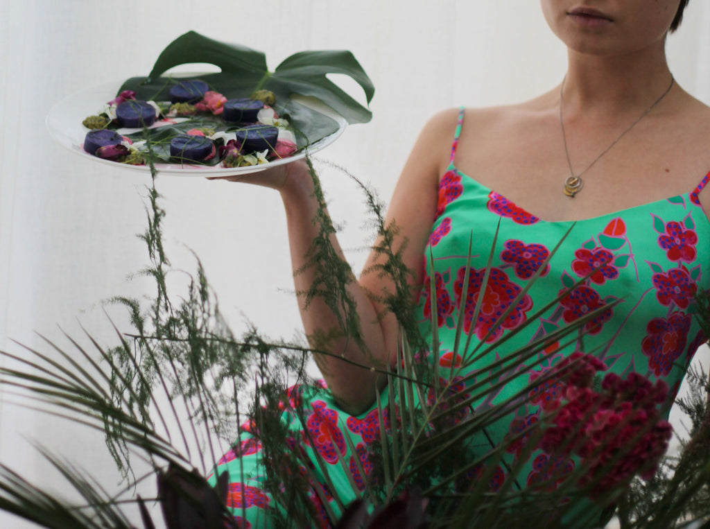 Kay Kimura-Dickson in Crimson Rose green floral print slip dress holding starter plate she designed and prepared as part of our Island Dreams collection collaboration with 0K Studios.