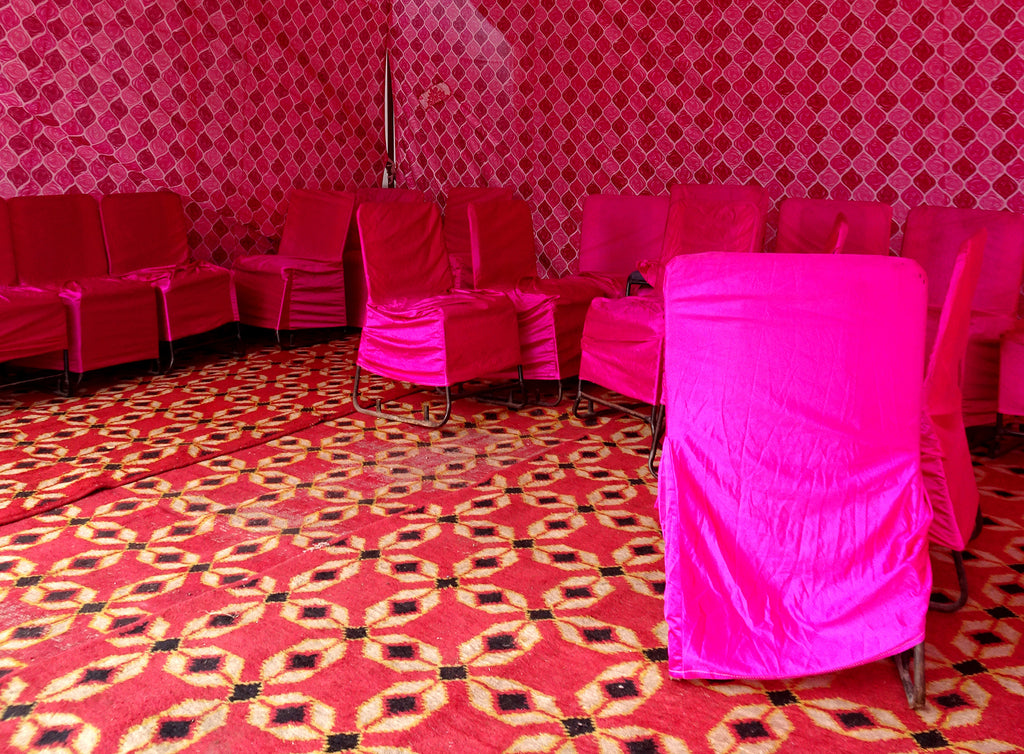 Chairs in India covered in bright pink fabric in a room with highly patterned pink flooring and walls.