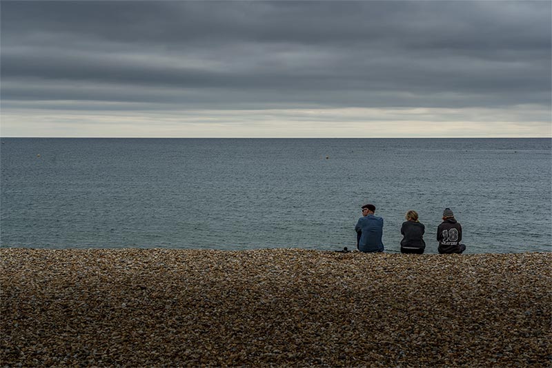 Trois personnes assises sur Lyme Regis Shingle Beach 