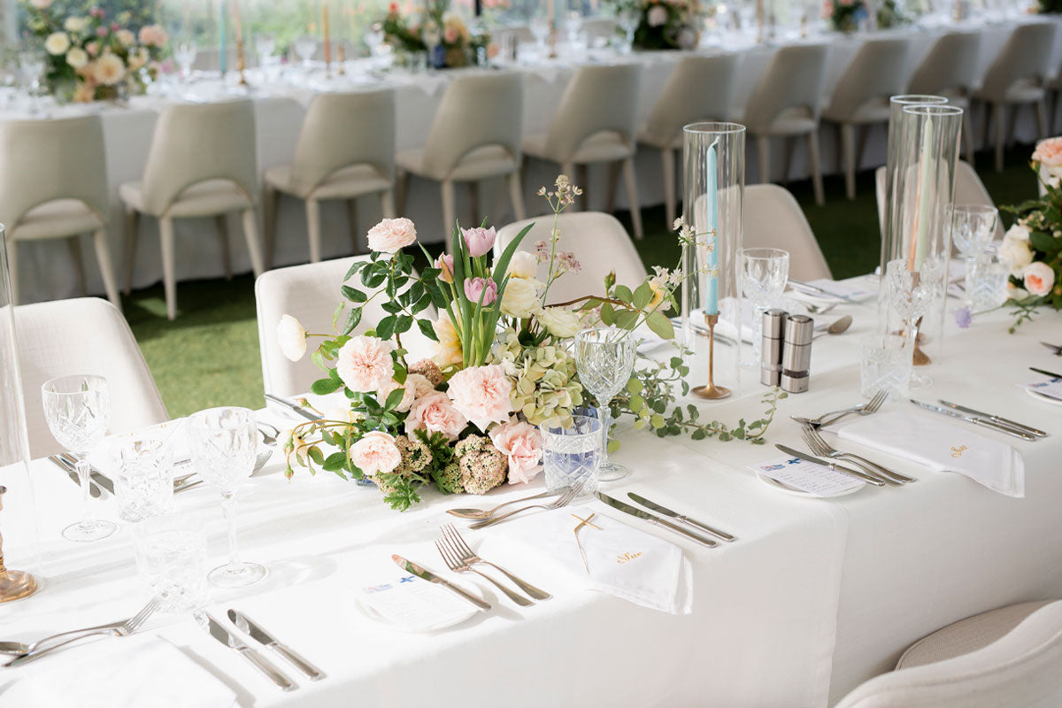 A dining table for a wedding with white table cloths, crystal rocks and champaign glasses and a table flower bouquet  