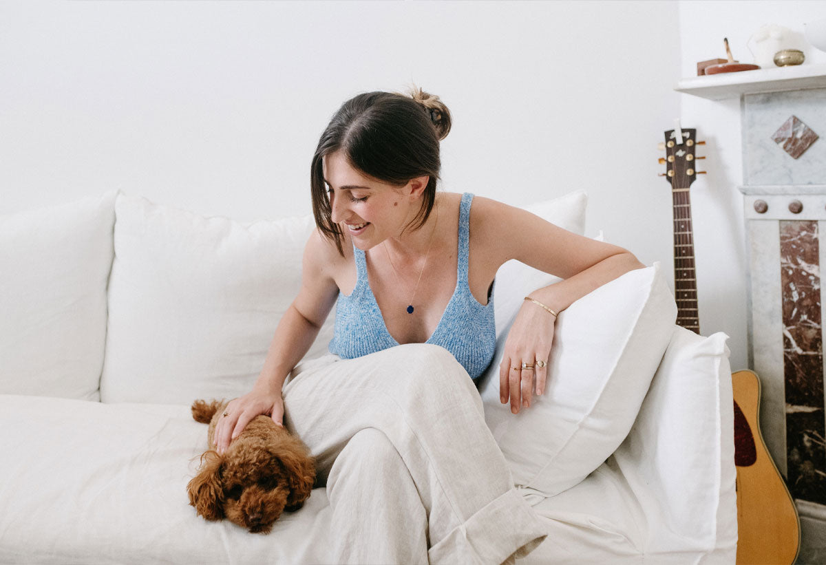 Amanda Bardas wearing a light blue top and sitting on a white couch while stroking her dog's head