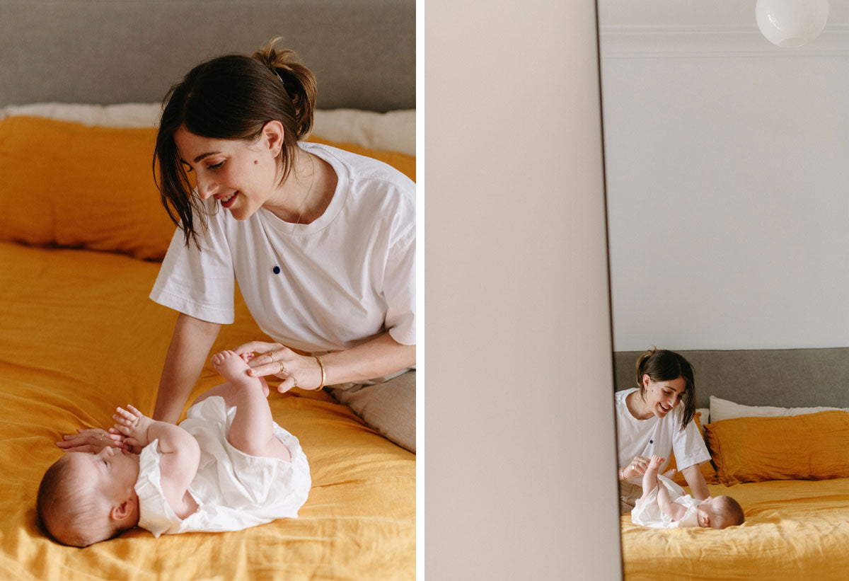 Amanda Bardas and her baby daughter smiling and sitting and lying on a bed with a yellow bed sheet