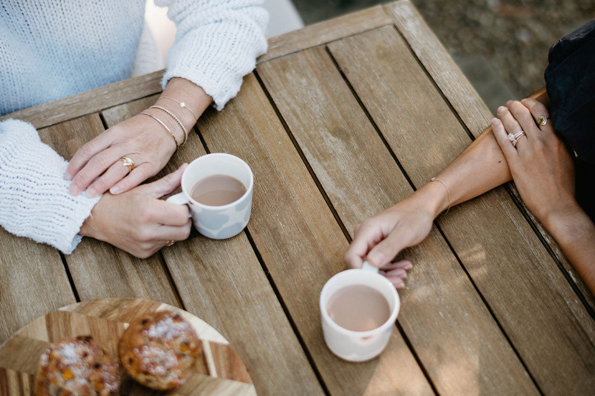 A close up of Zinovia's and Julia's hands holding a cup of tea and both wearing a Polaris Bracelet handmade by Natalie Marie Jewellery