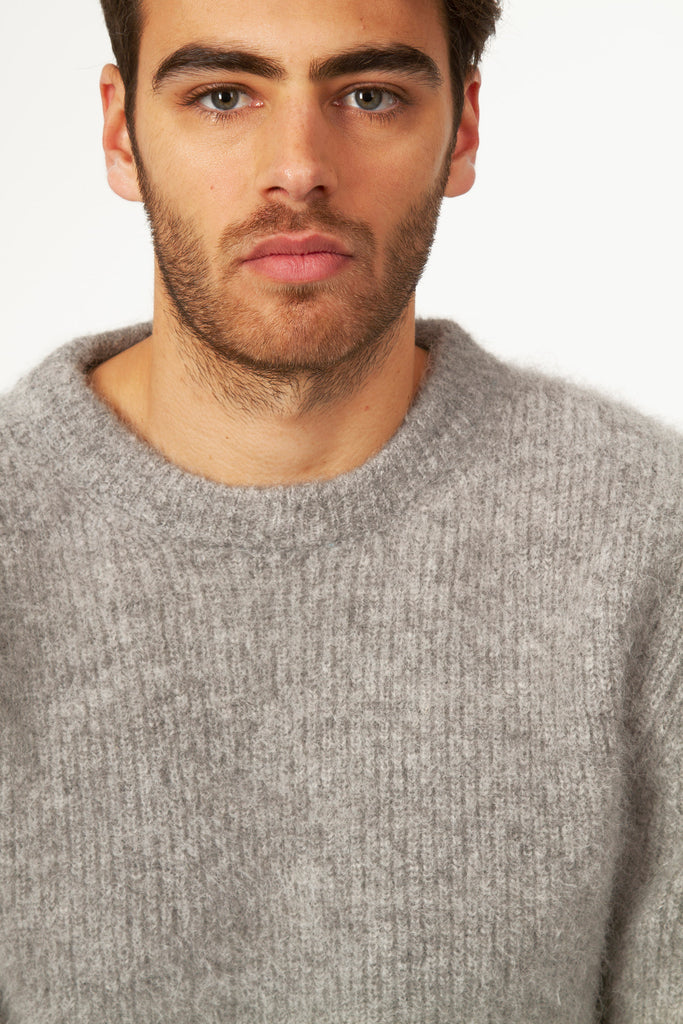 Young man with three day beard wearing light gray chunky knit crew neck sweater made of warm and soft alpaca wool for the season