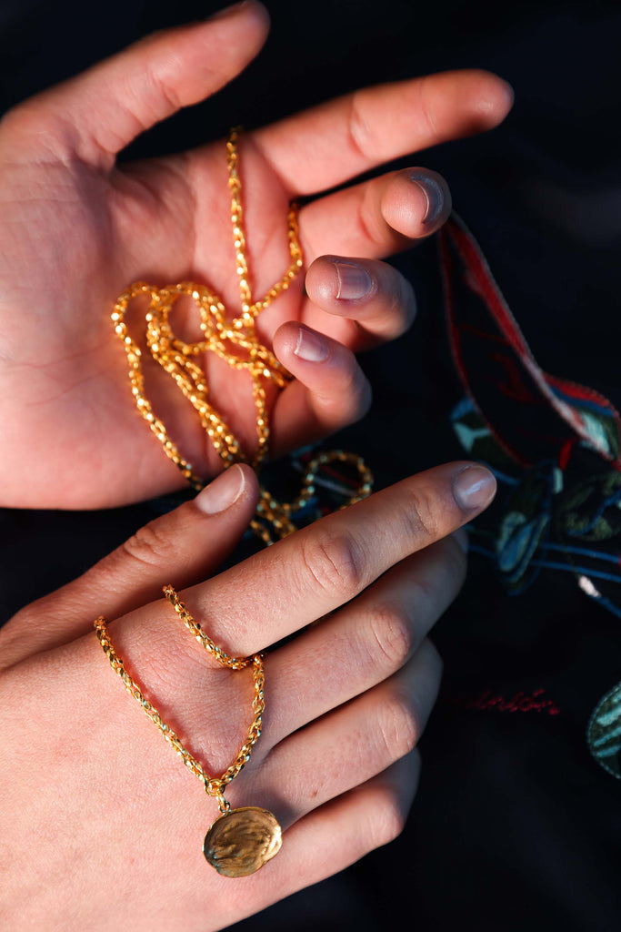 Close-up of hands holding a delicate golden chain necklace made in an artisanal way