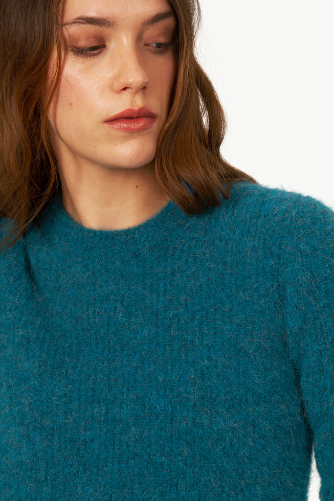 Young woman looking aside in lagoon blue knit sweater in thick textured crew neck in alpaca knit unique know-how ethical Peruvian tailoring