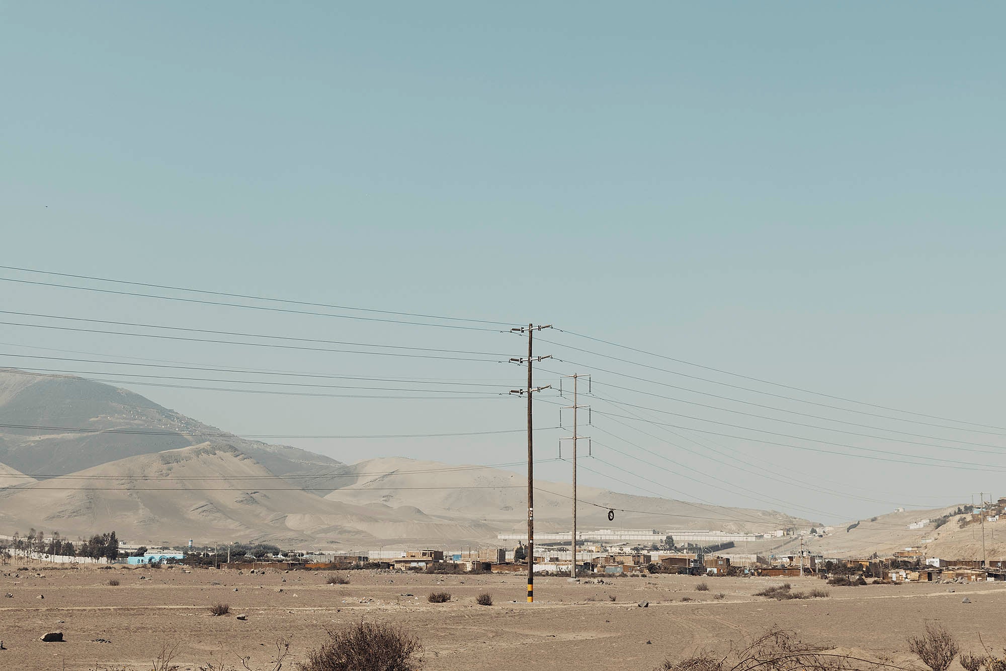 Poteau électrique photographié par devant des bidonvilles et montagnes de sable visibles en arrière plan