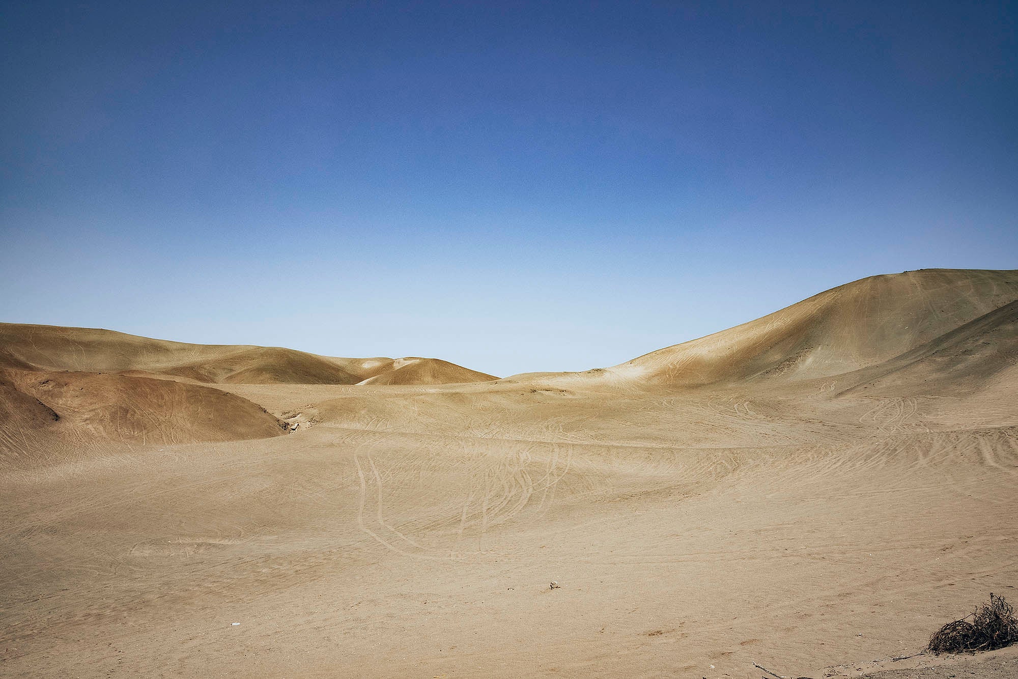 Desert with sand dunes in the background and tire tracks on the sand