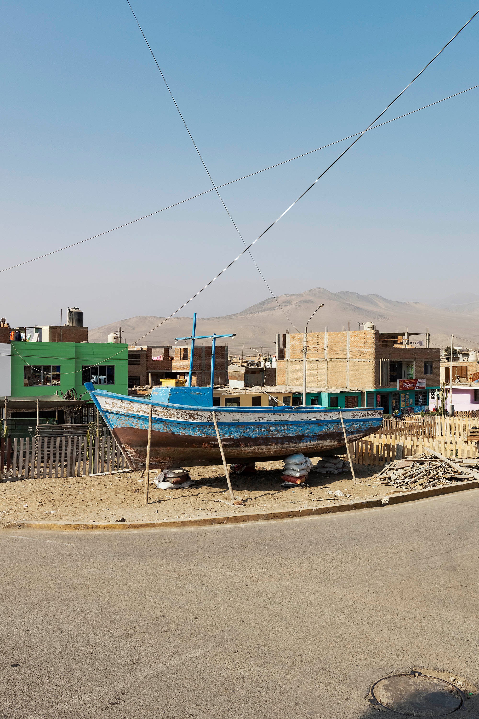 Wooden boat held by sticks and bags photographed in front of slums