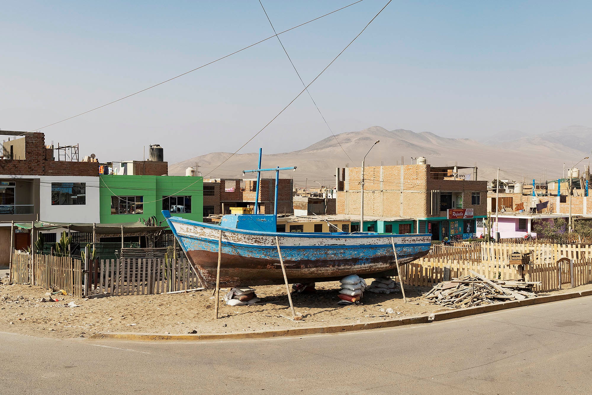 Barque en bois maintenue par des bâtons et des sacs photographié par devant des bidonvilles
