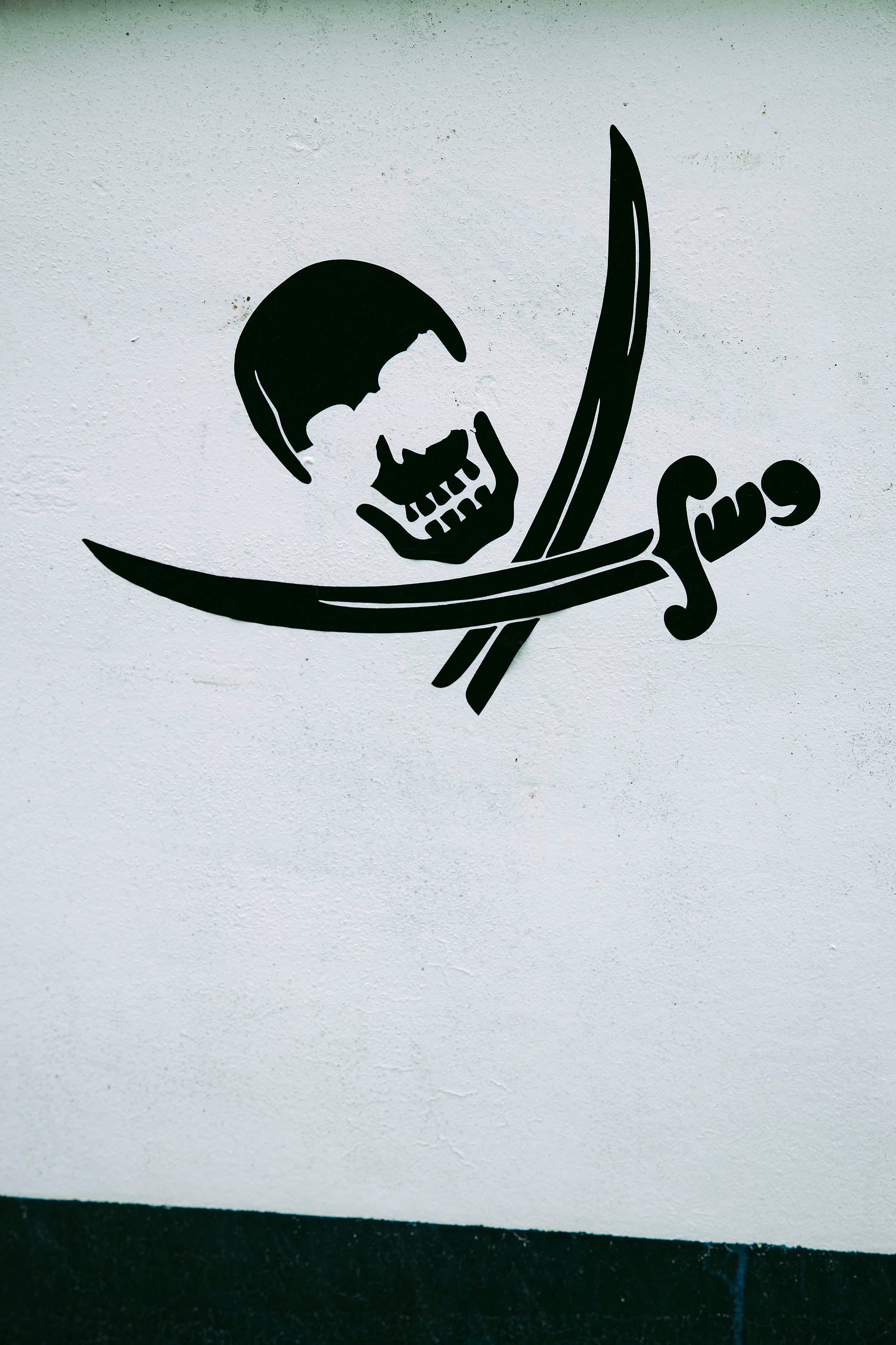 Tag tête de mort avec un sabre et son fourreau dessiné en bas de son crâne taggé sur un mur blanc