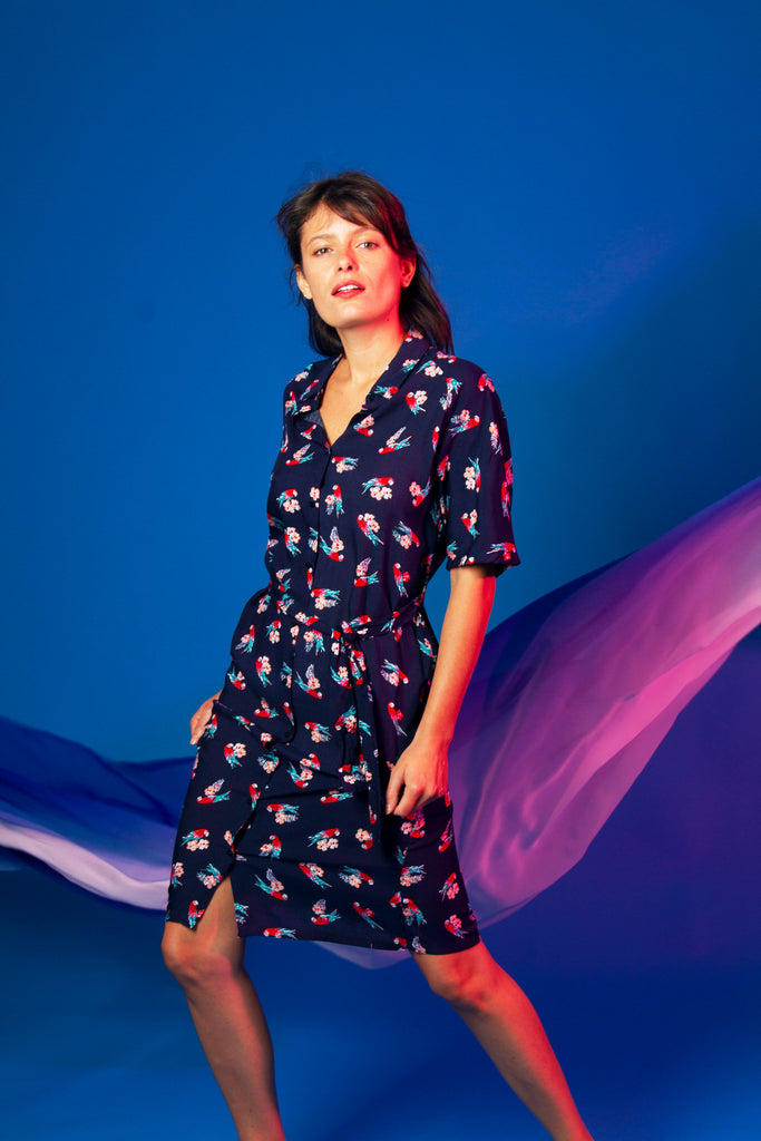Dark-haired woman with a curtain bang in a short-sleeved dress with a button and a navy blue midi belt with an exotic nature-inspired parrot print