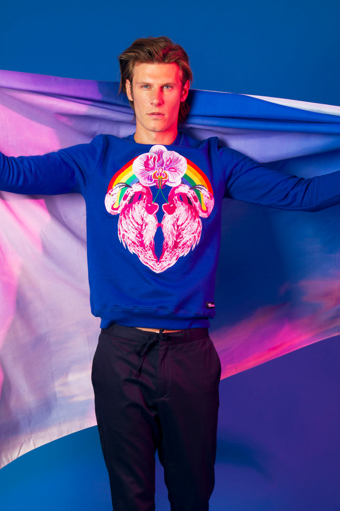 Blue-eyed man with embroidered round-neck cotton sweatshirt with pink flamingos on the front bright colors LGBT+ flag committed collection