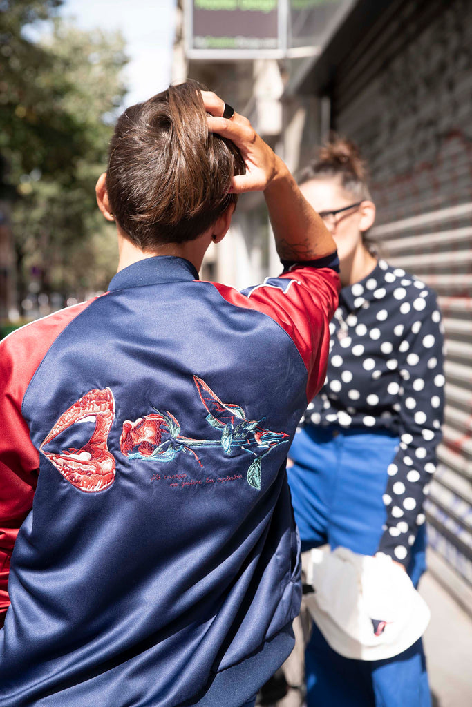 Young woman from behind pixie cut wearing a satin jacket and feminist embroidery