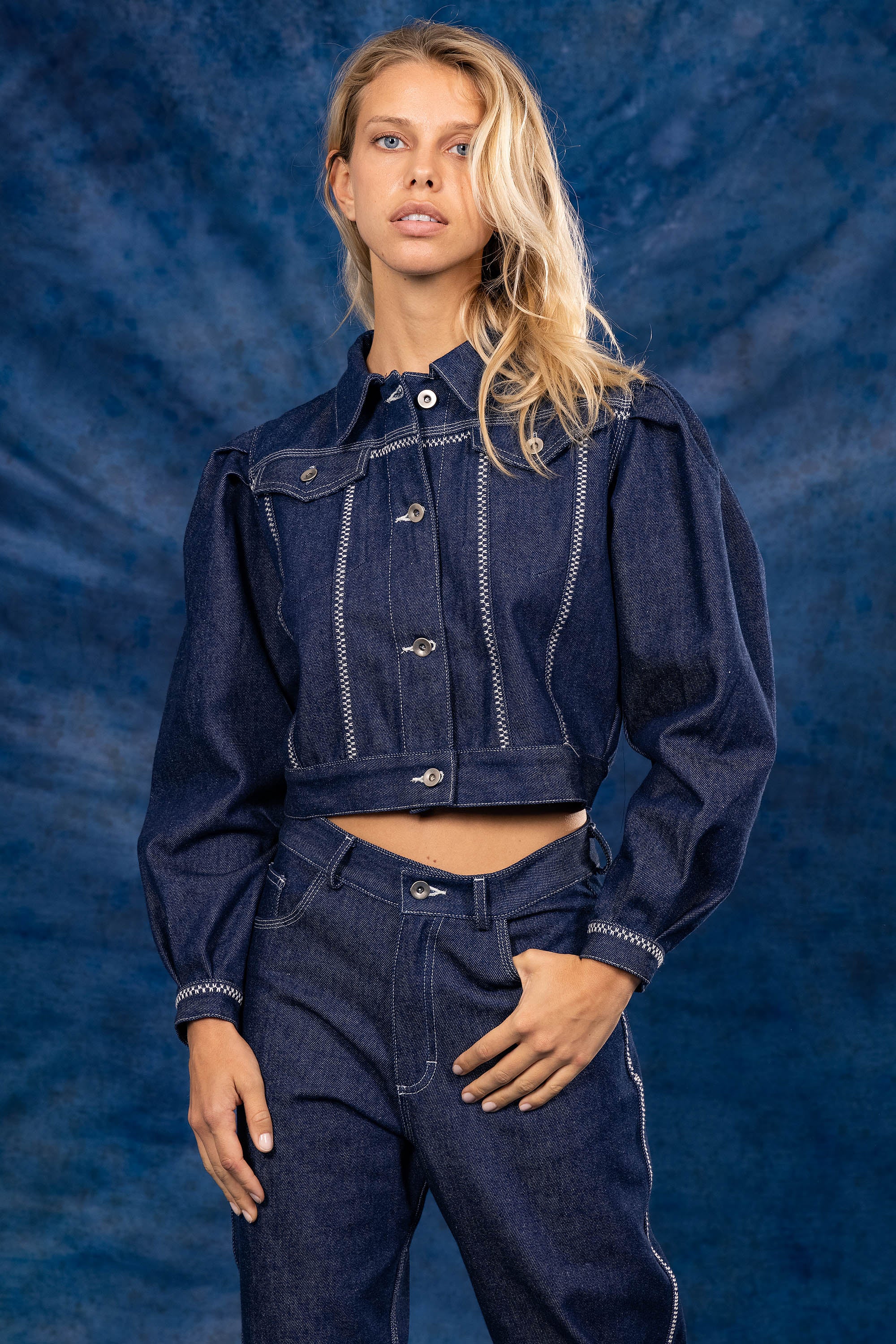 femme portant une veste bleu denim avec le pantalon assorti sur fond bleu nouvelle collection été 2023 misericordia