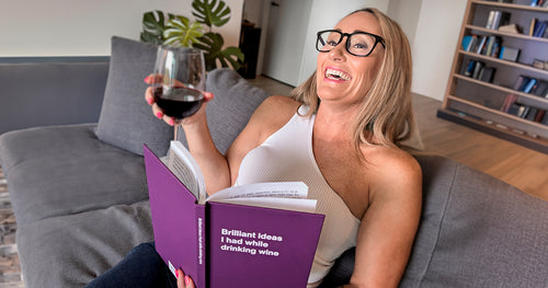A woman holding a glass of wine and a WTF Notebook, laughing