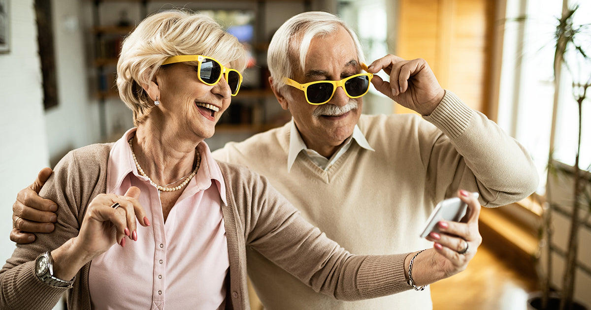 A senior couple wearing funny glasses and laughing at a smartphone