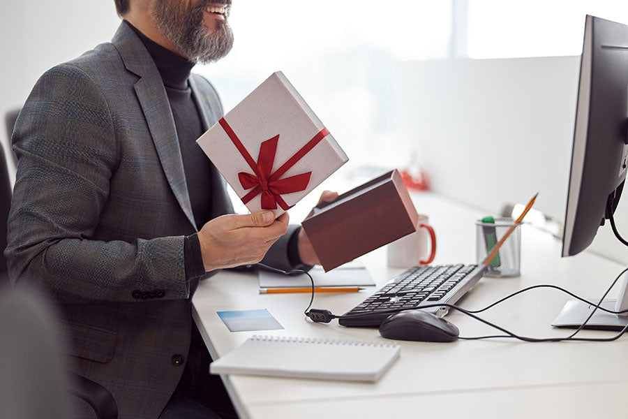 A man sitting at his desk, laughing while opening a corporate gift