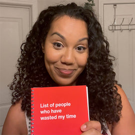 A happy customer holding her red WTF Notebook titled 'List of people who have wasted my time'