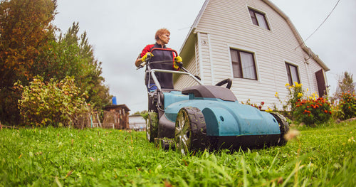 A woman pushing a lawnmower in her yard