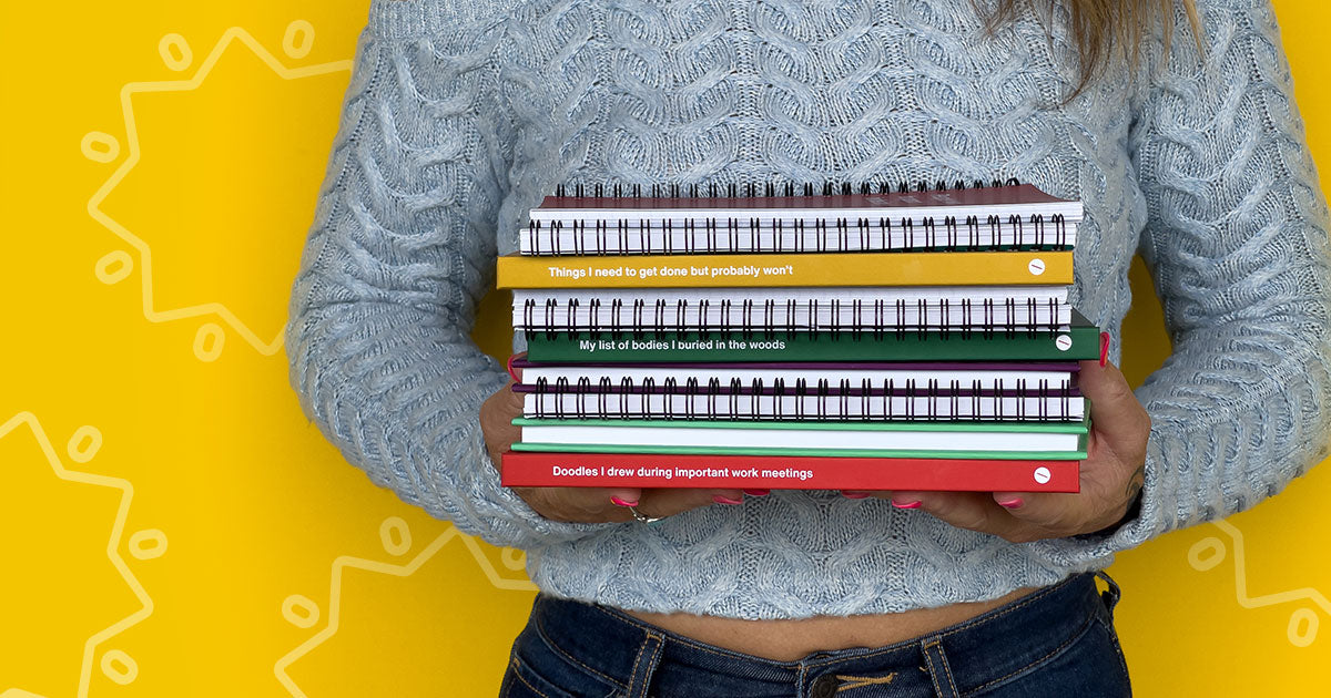 A woman holding a stack of 10 WTF Notebooks
