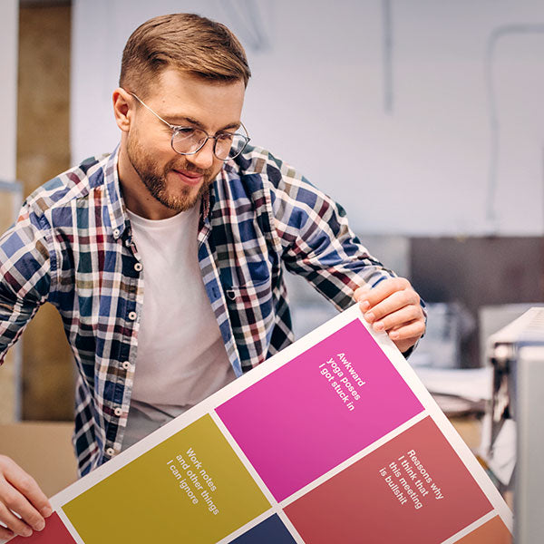 A young man in the WTF Notebooks print house, holding a sheet of notebook covers