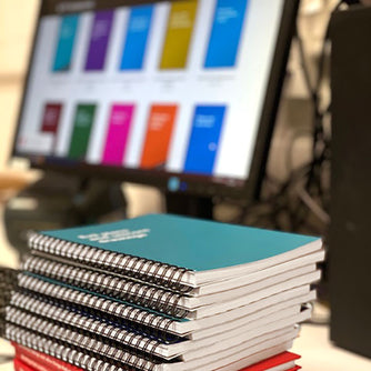 A stack of WTF Notebooks in front of a monitor