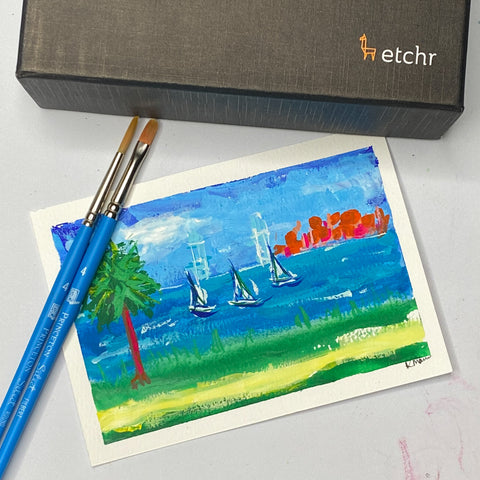 watercolor postcards, paintbrush and a postcard with sailboats on it