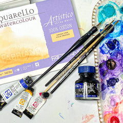 photo of watercolor block of paper, watercolor paint in tubes, brushes, calligraphy ink and pen and pallet
