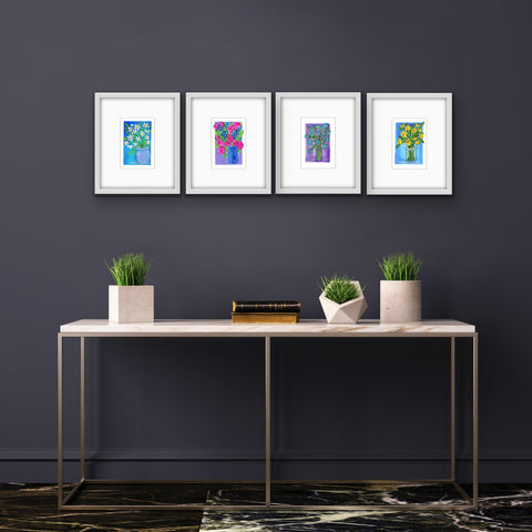 4 gouache floral paintings matted and framed above a metal end table with small plants 