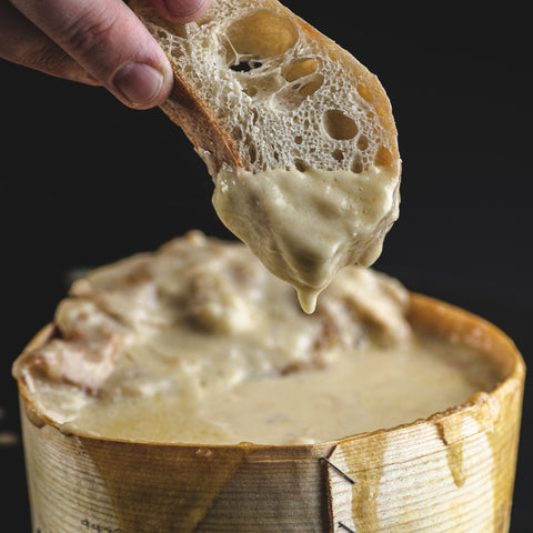 Dipping a piece of baguette into a molten wheel of Vacherin Mont d'Or from Switzerland.