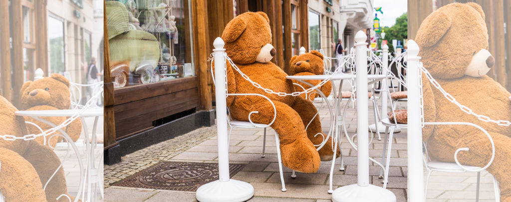 Oso de peluche gigante sentado en la terraza de una cafetería.