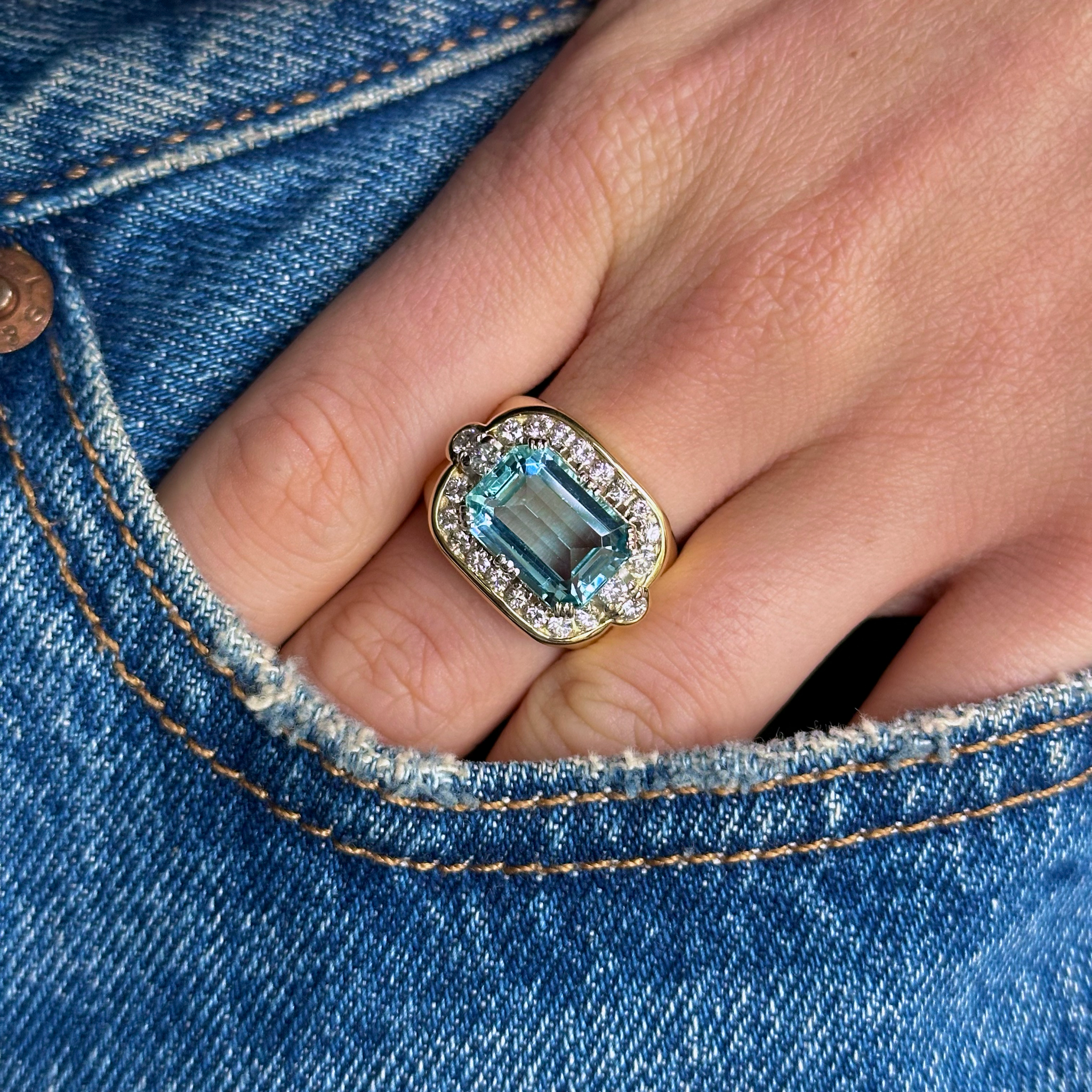 Aquamarine and diamond cluster cocktail ring worn on hand in pocket of jeans.