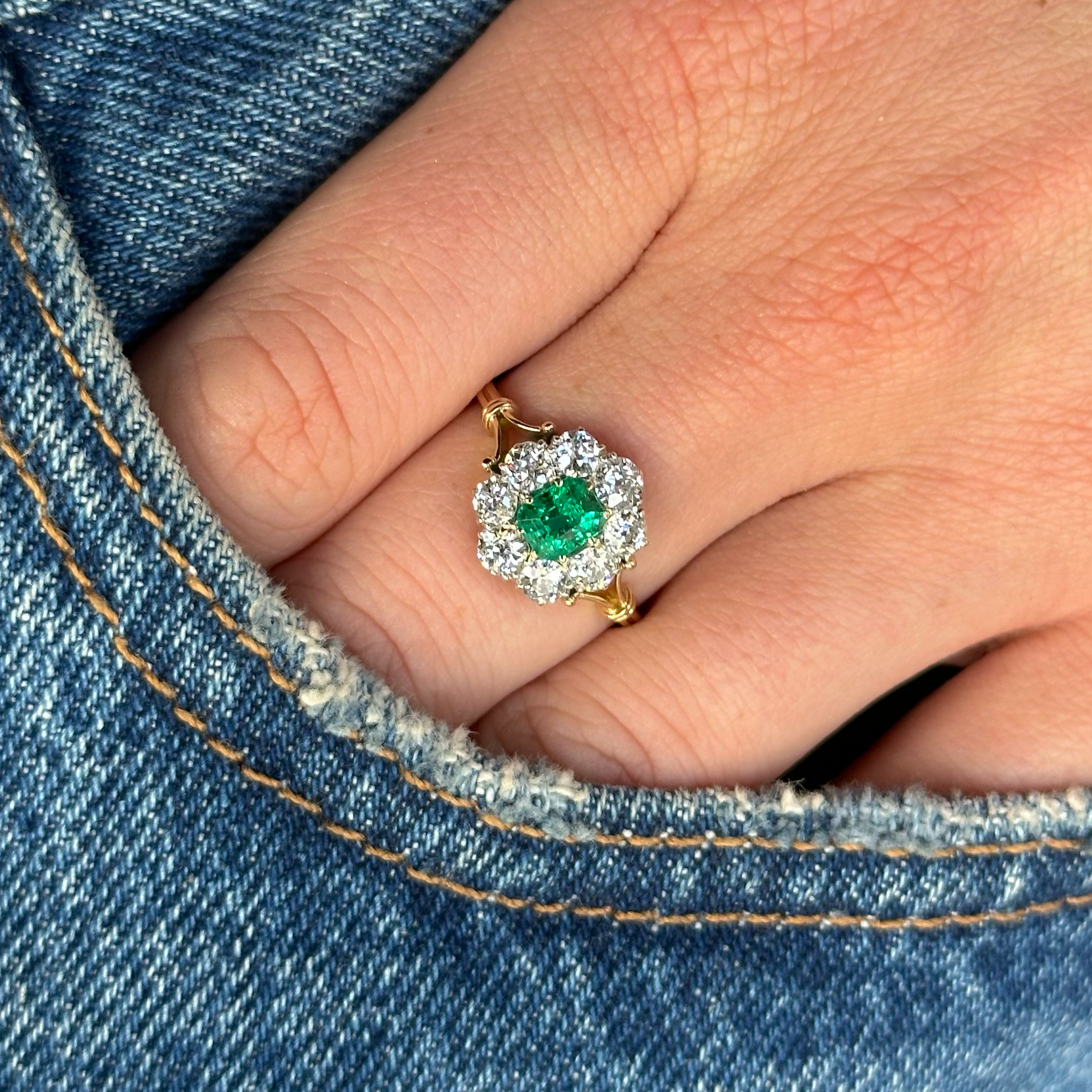 antique edwardian emerald and diamond cluster ring worn on hand in pocket of jeans.