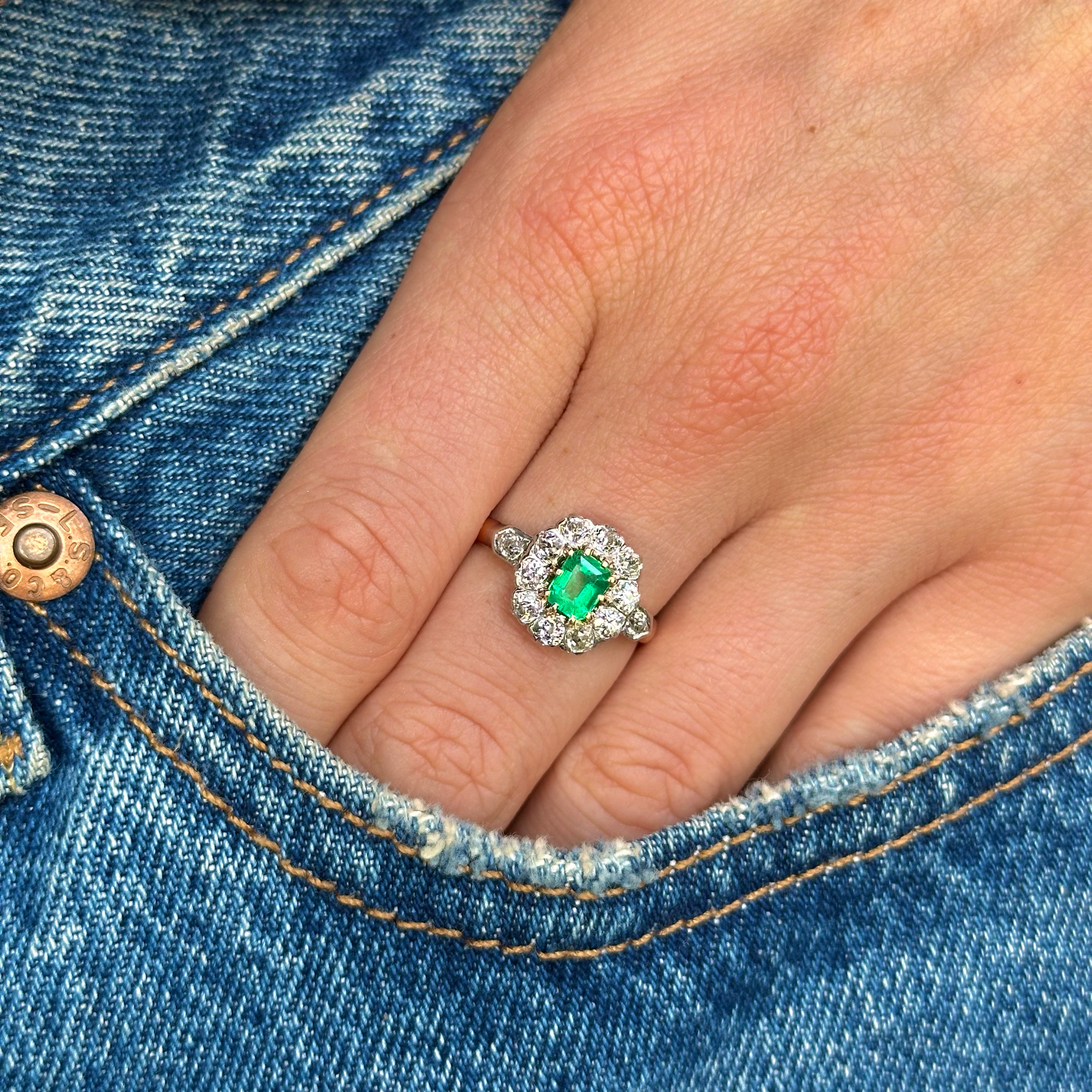 Antique emerald and diamond cluster ring worn on hand in pocket of jeans