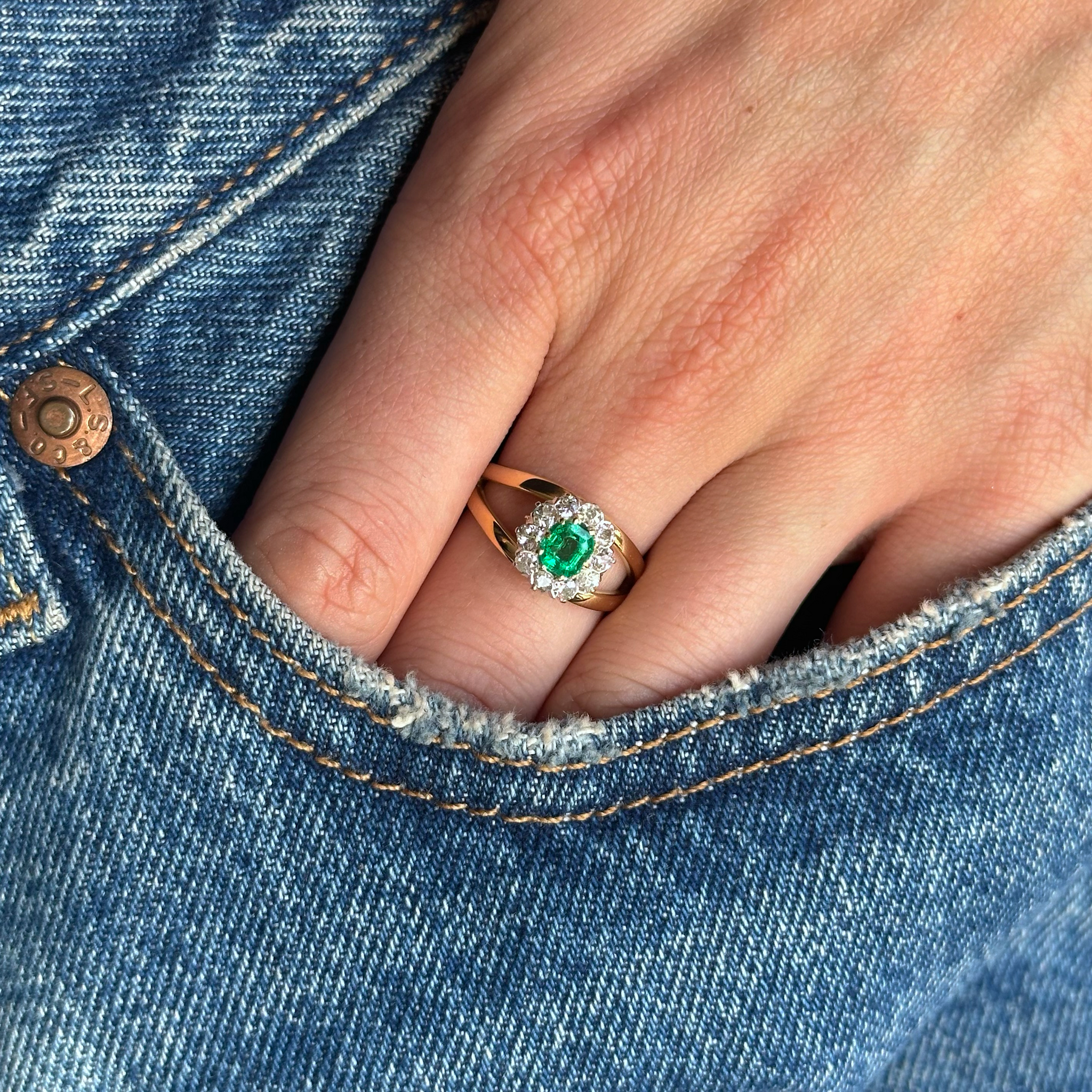 Emerald and diamond ring on hand inside pocket of jeans