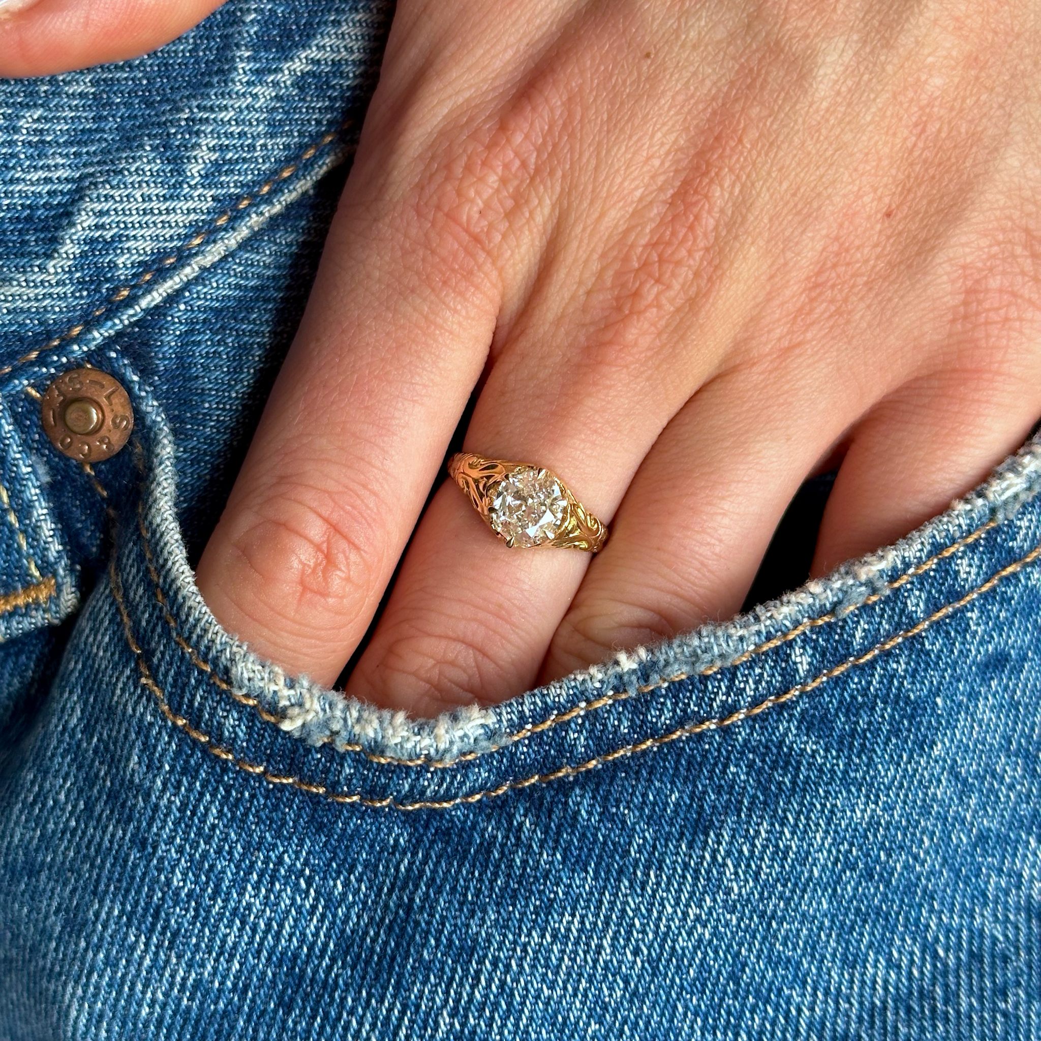 Diamond solitaire engagement ring worn on hand photographed in pocket of jeans
