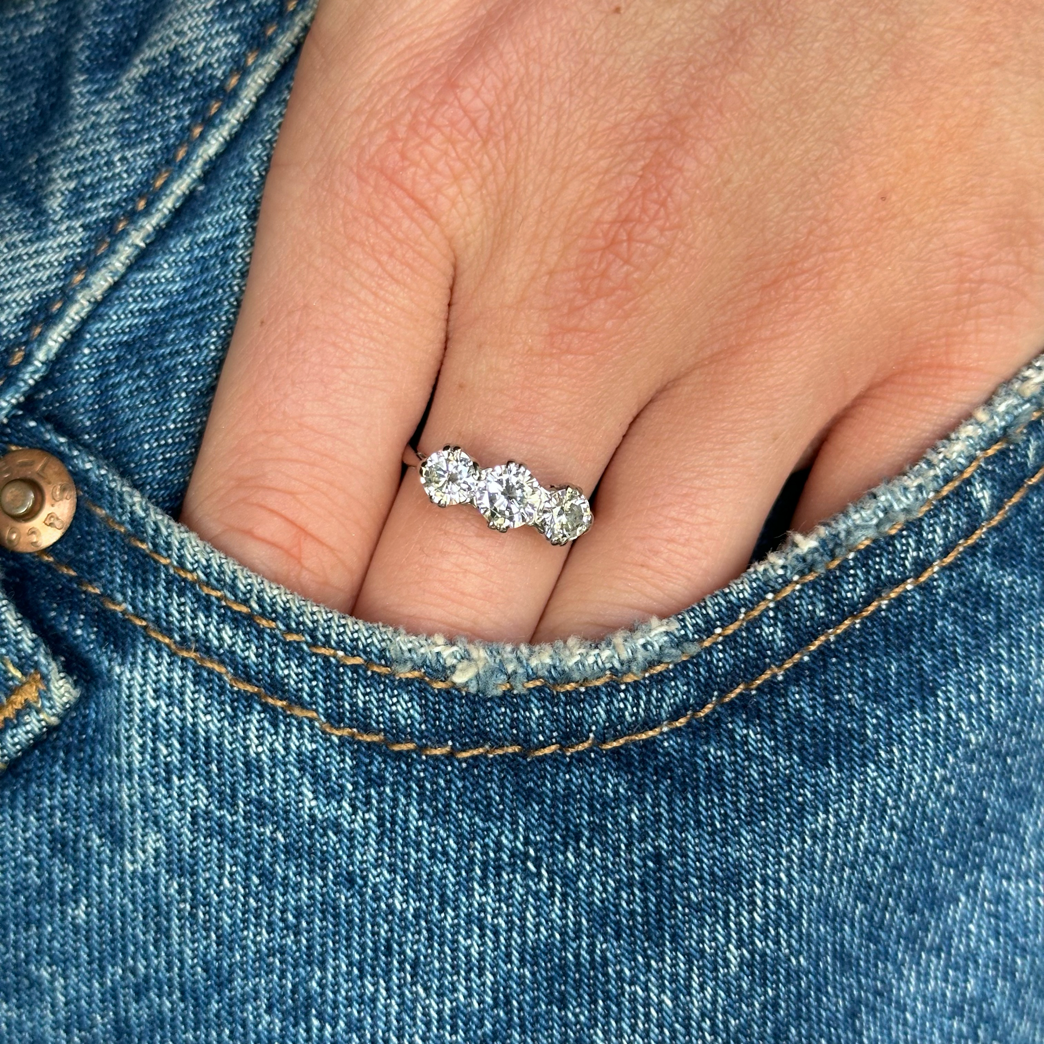 three stone diamond ring worn on hand in pocket of jeans.