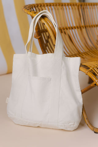Pehr Natural Canvas Tote Bag leaning next to woven chair