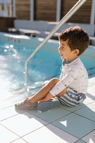 Little boy by a pool with a swim Rash Gaurd and shorts on