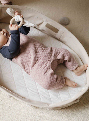 baby laying in basket on floor playing with teether